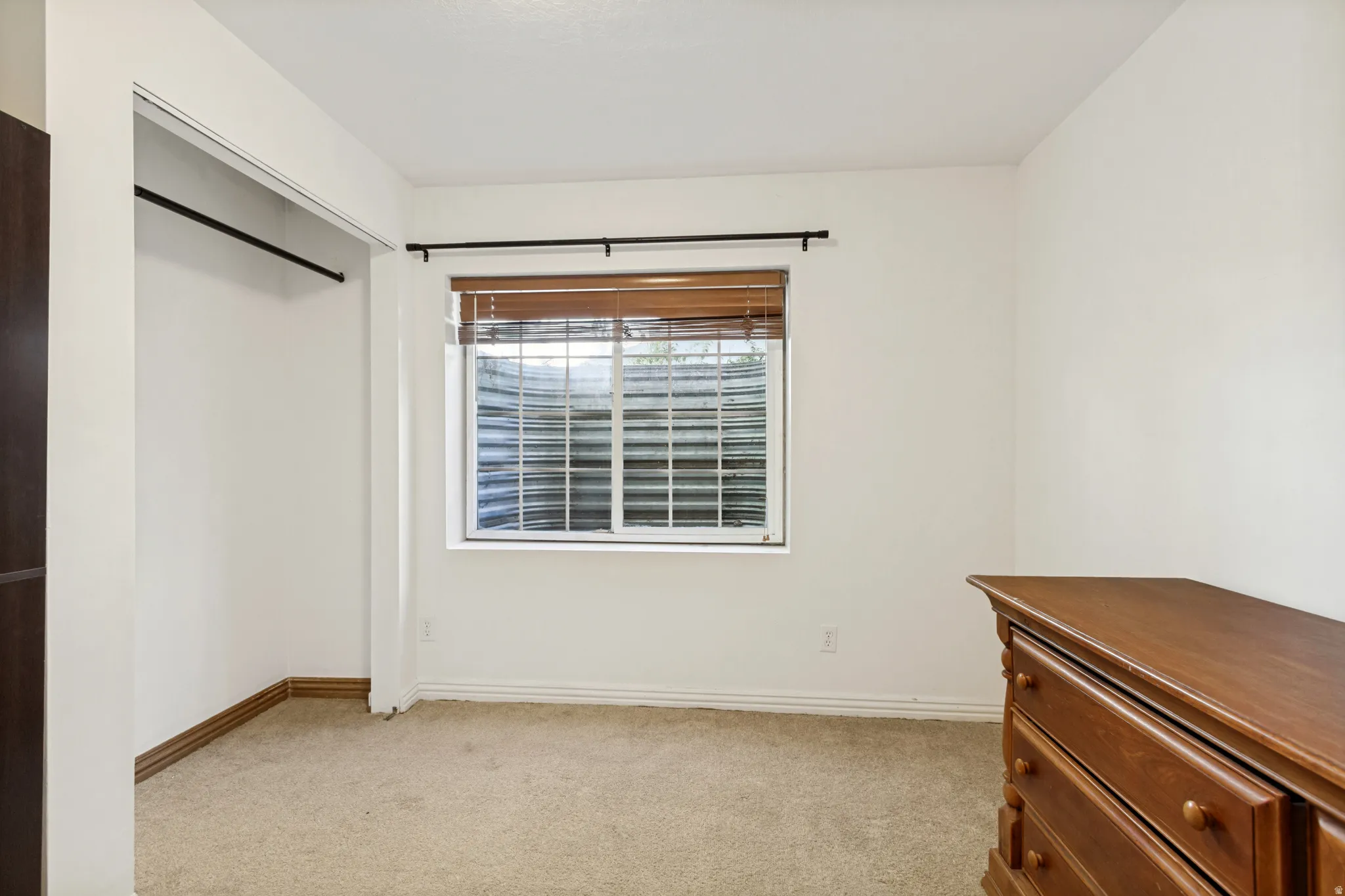 Carpeted room with a window featuring wood-finish blinds and a metal window well