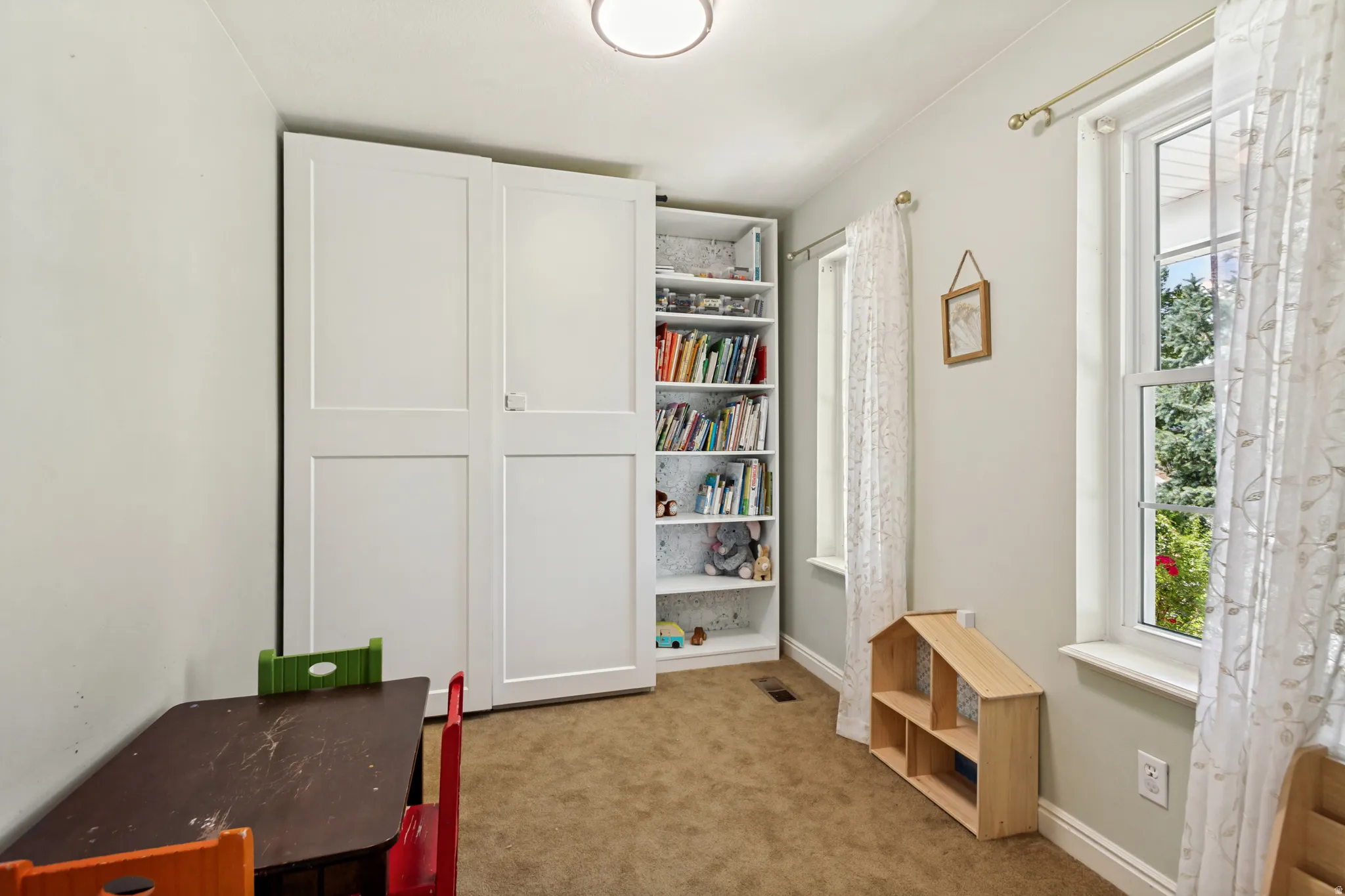 Built-in shelving with concealed storage, two double-hung windows, and a flush-mount ceiling light