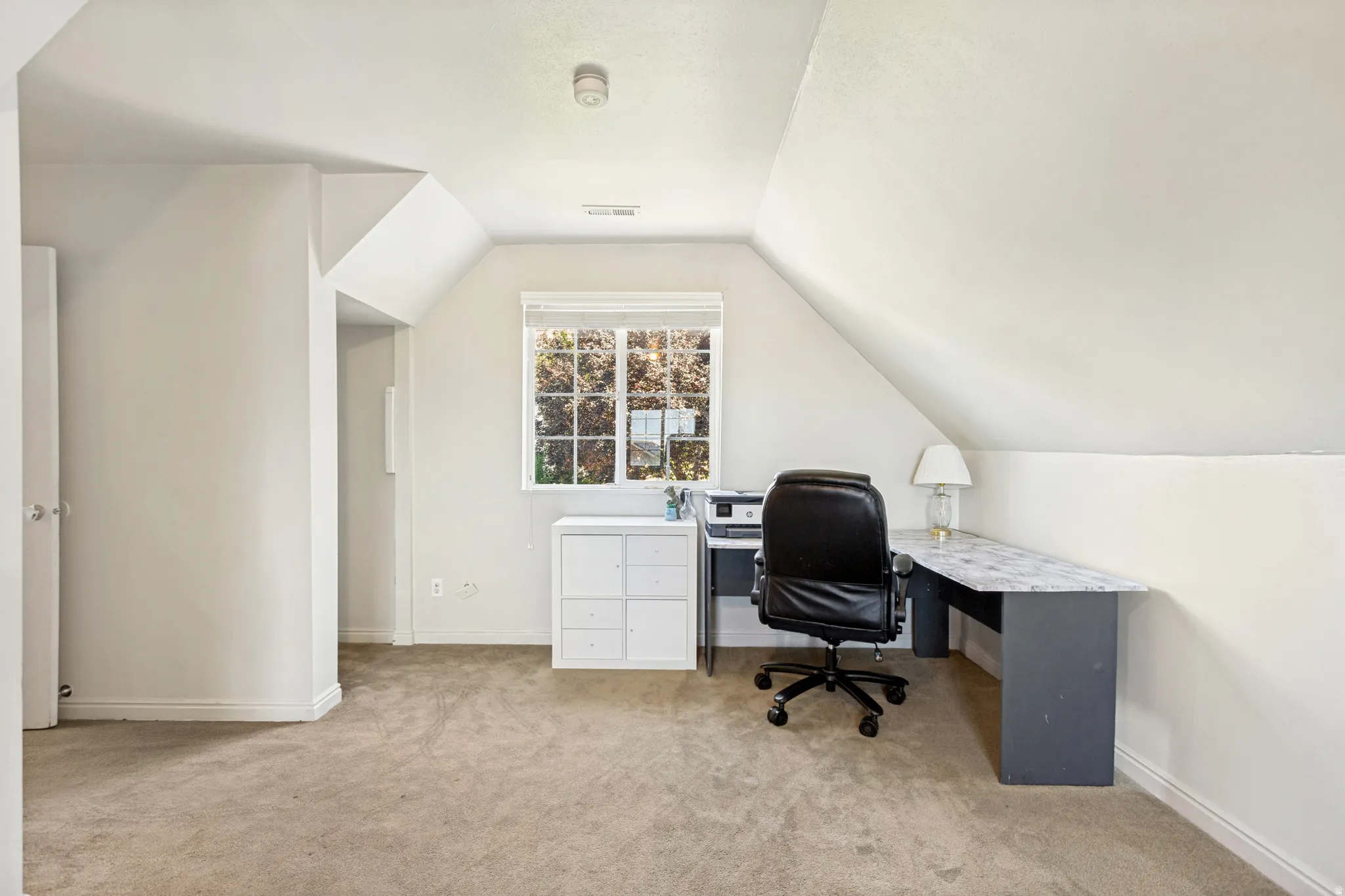 Carpeted room featuring an angled ceiling, a window with white trim, and a built-in desk with a light-colored countertop
