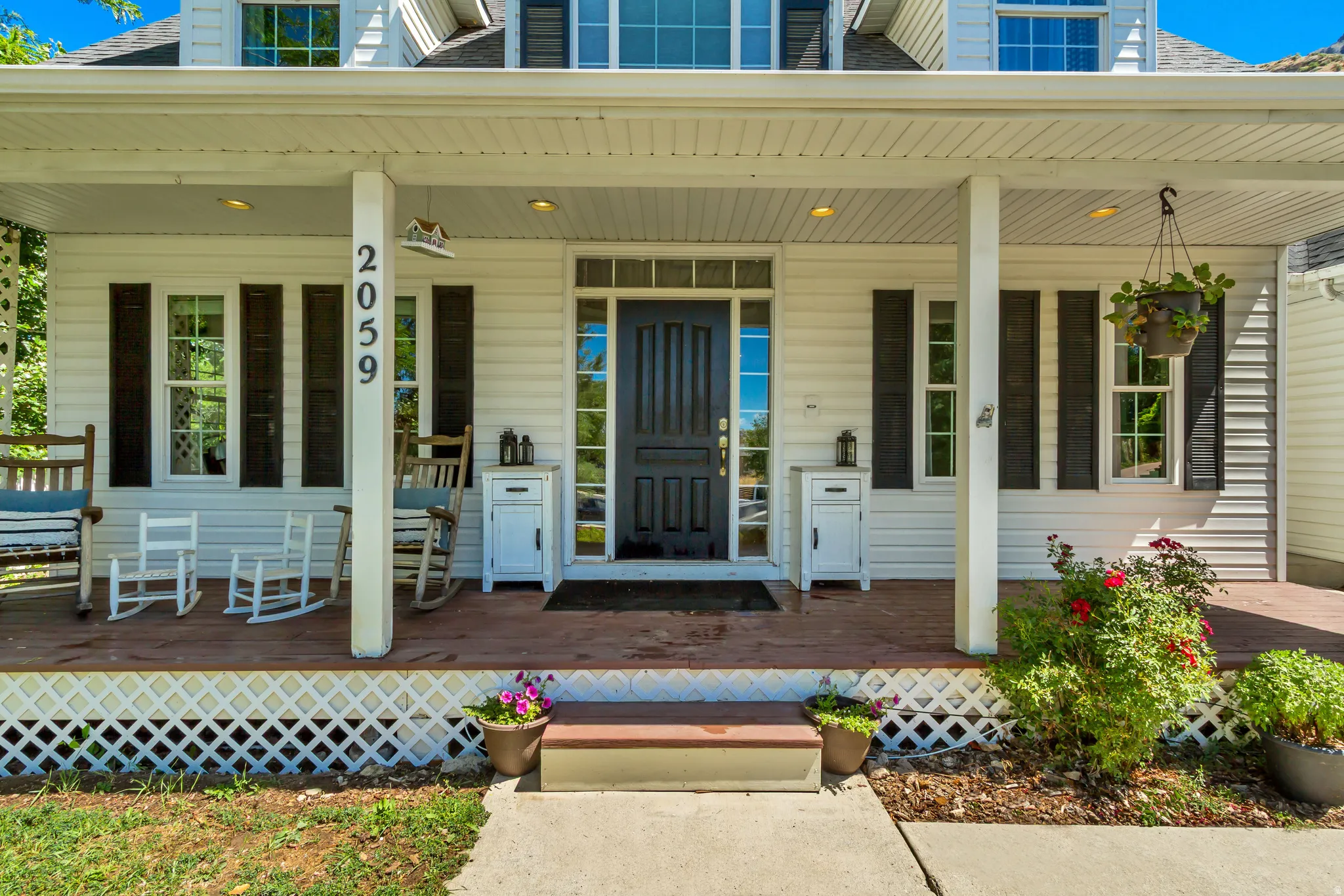 Inviting covered front porch with recessed lighting, dark wood-finish flooring, white siding, and contrasting black shutters