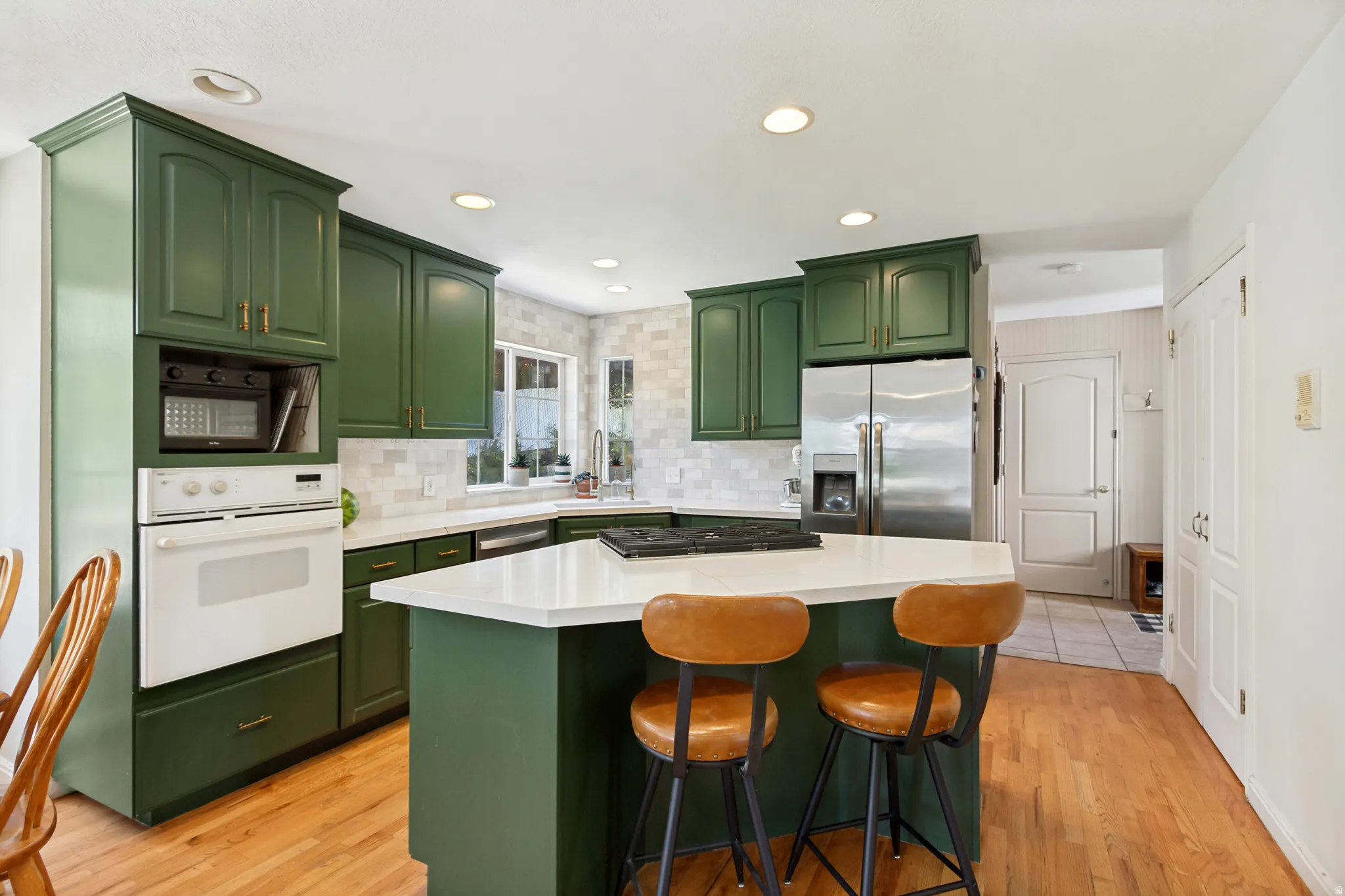 Kitchen featuring green cabinetry, white countertops, built-in appliances, stainless steel refrigerator, and wood-finish flooring