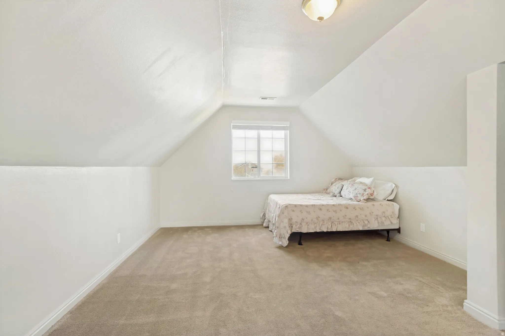 Carpeted room with a pitched ceiling, recessed wall feature, window with horizontal blinds, and a semi-flush mount ceiling light