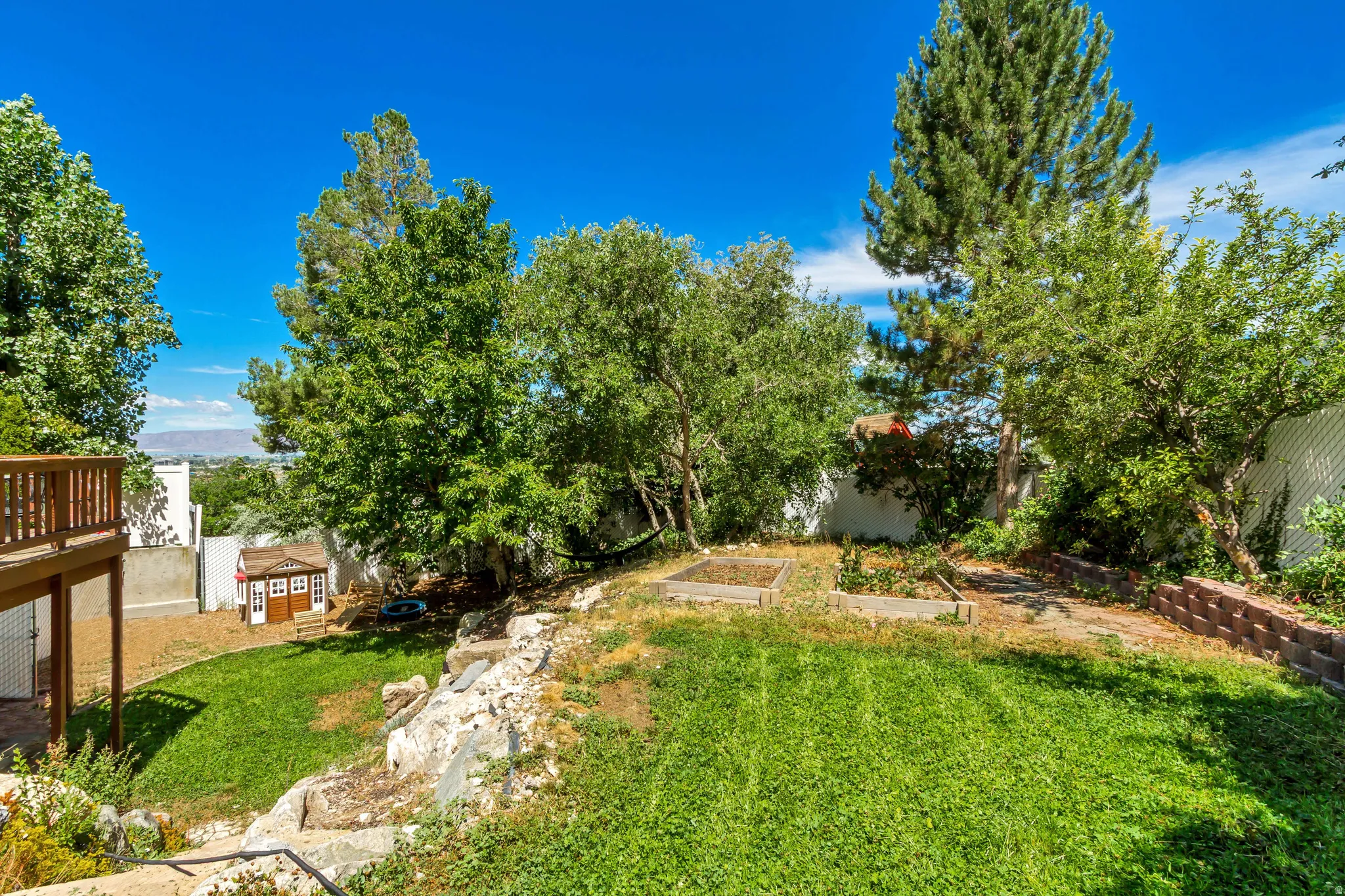 Expansive terraced backyard featuring a wood deck, mature trees, a lower lawn area, and raised garden beds