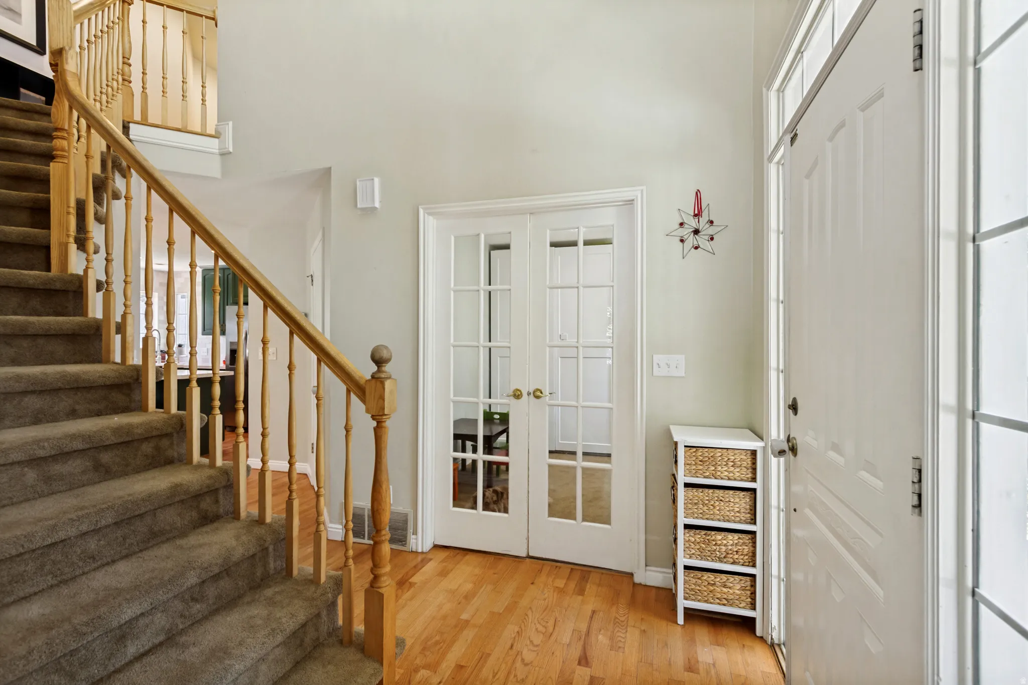 Foyer featuring wood-finish flooring, a carpeted staircase with a light wood baluster and handrail, a white paneled entry door with transom and sidelight windows, and French doors with glass panes
