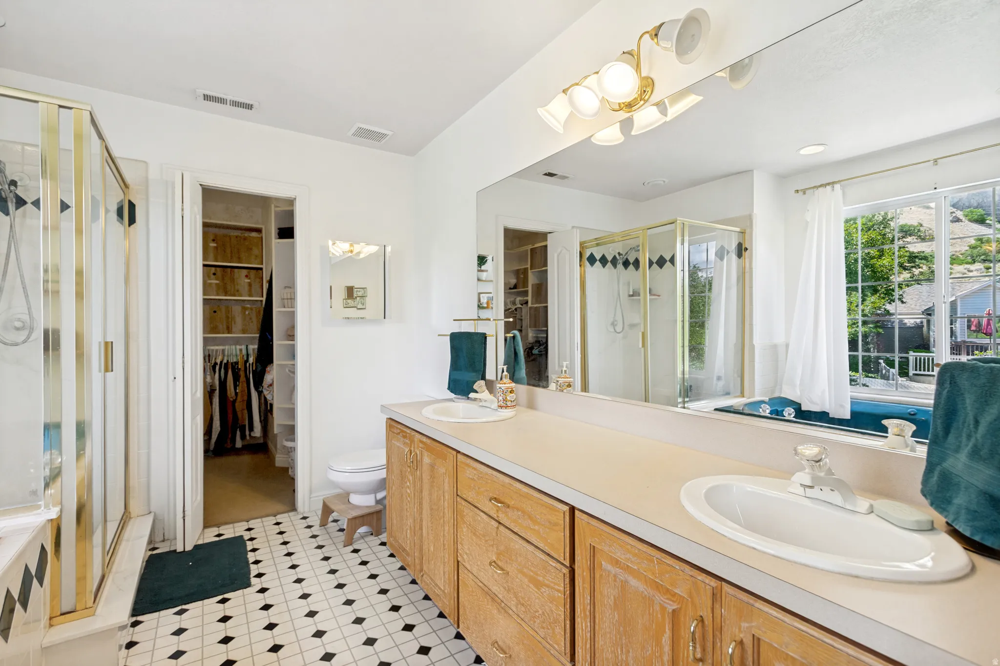Bathroom featuring a dual vanity with wood cabinetry, a built-in shower with clear glass enclosure, a soaking tub, and a walk-in closet with shelving