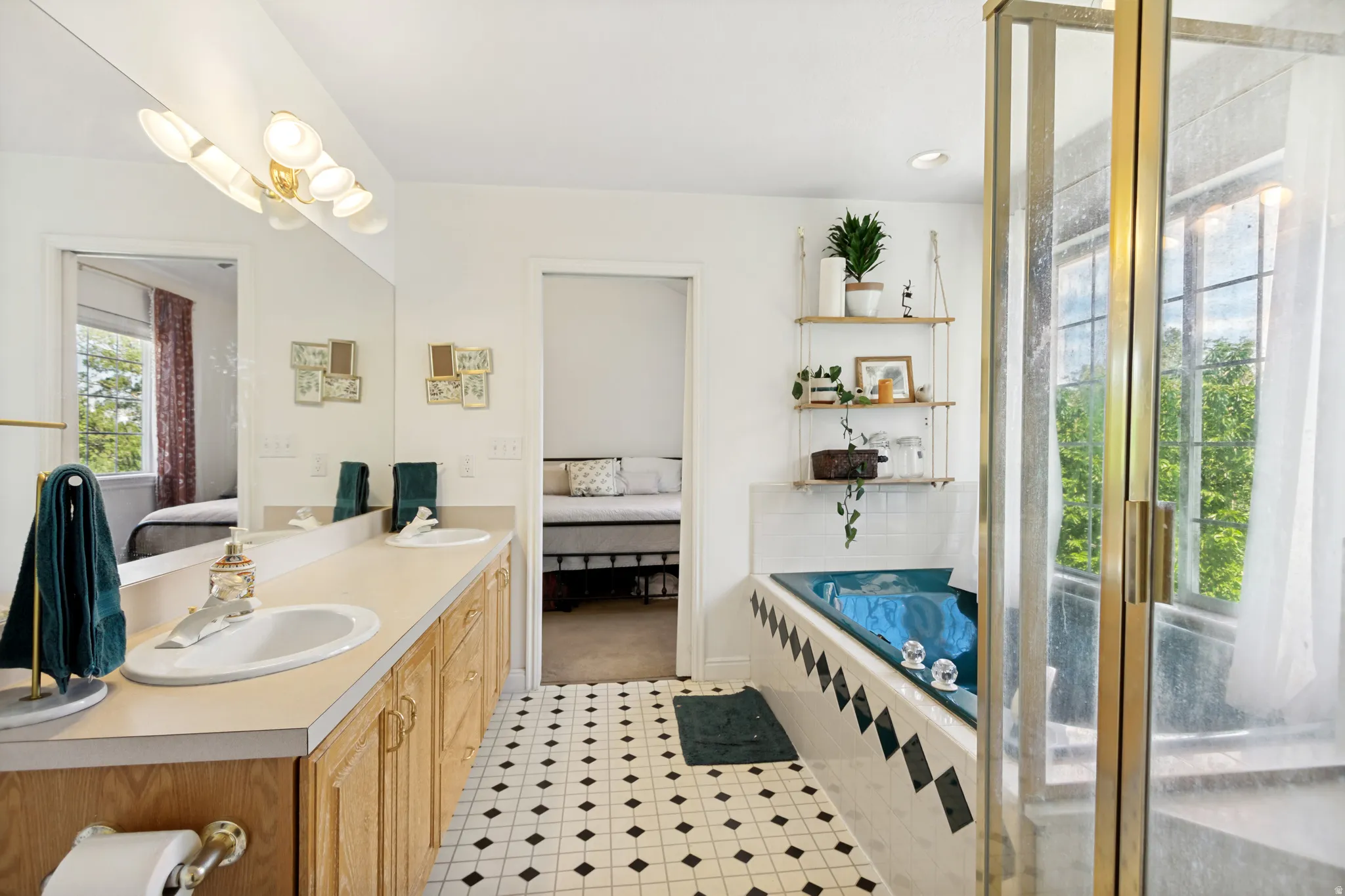 Bathroom featuring a dual vanity with light wood cabinetry and integrated sinks, a built-in soaking tub with black and white tile surround, a glass-enclosed shower, and black and white patterned floor tiles