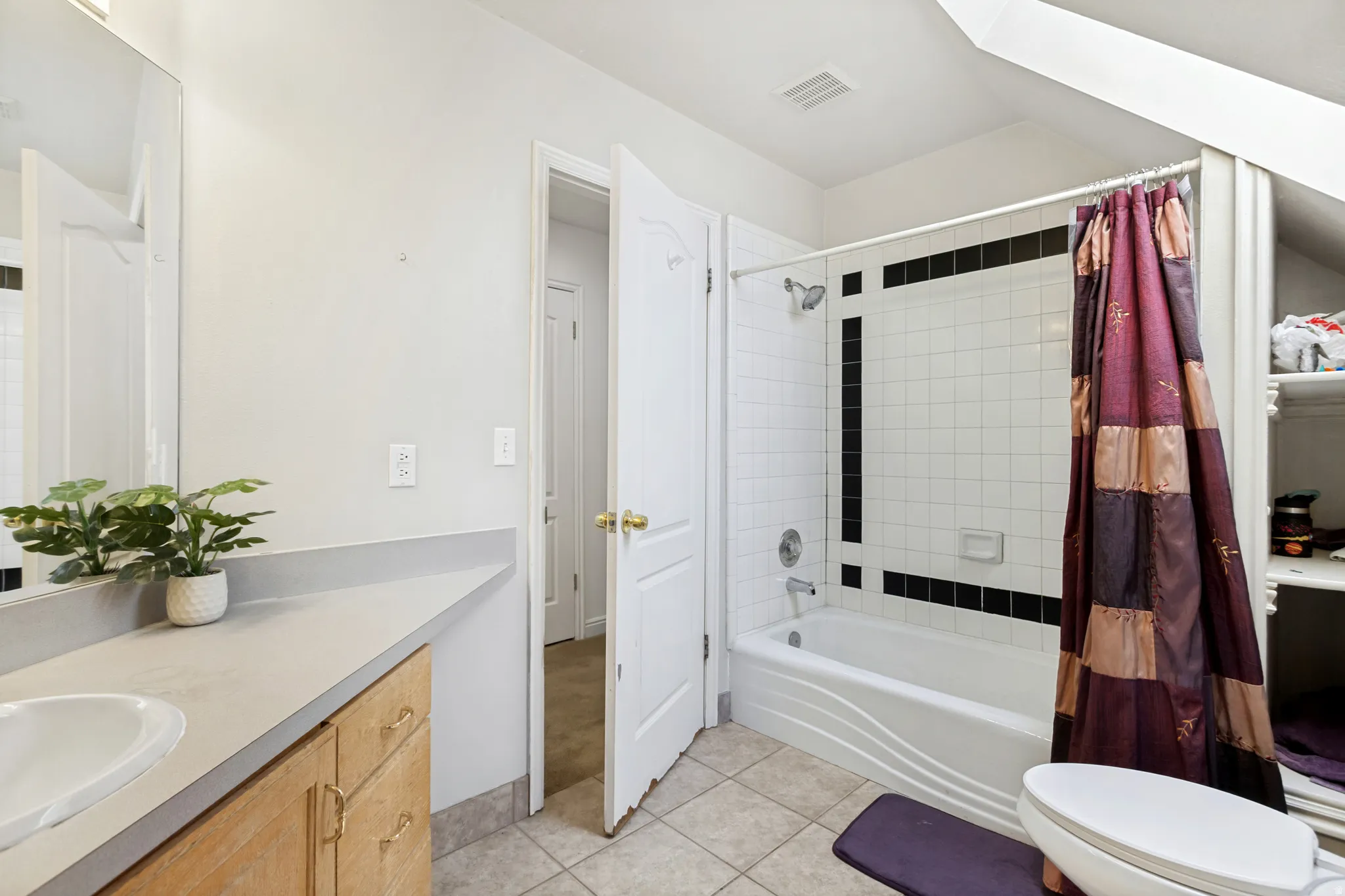 Bathroom featuring a white subway tile shower with black accent tiles, a built-in tub, a light wood-finish vanity with a single sink, a large wall mirror, and tile flooring