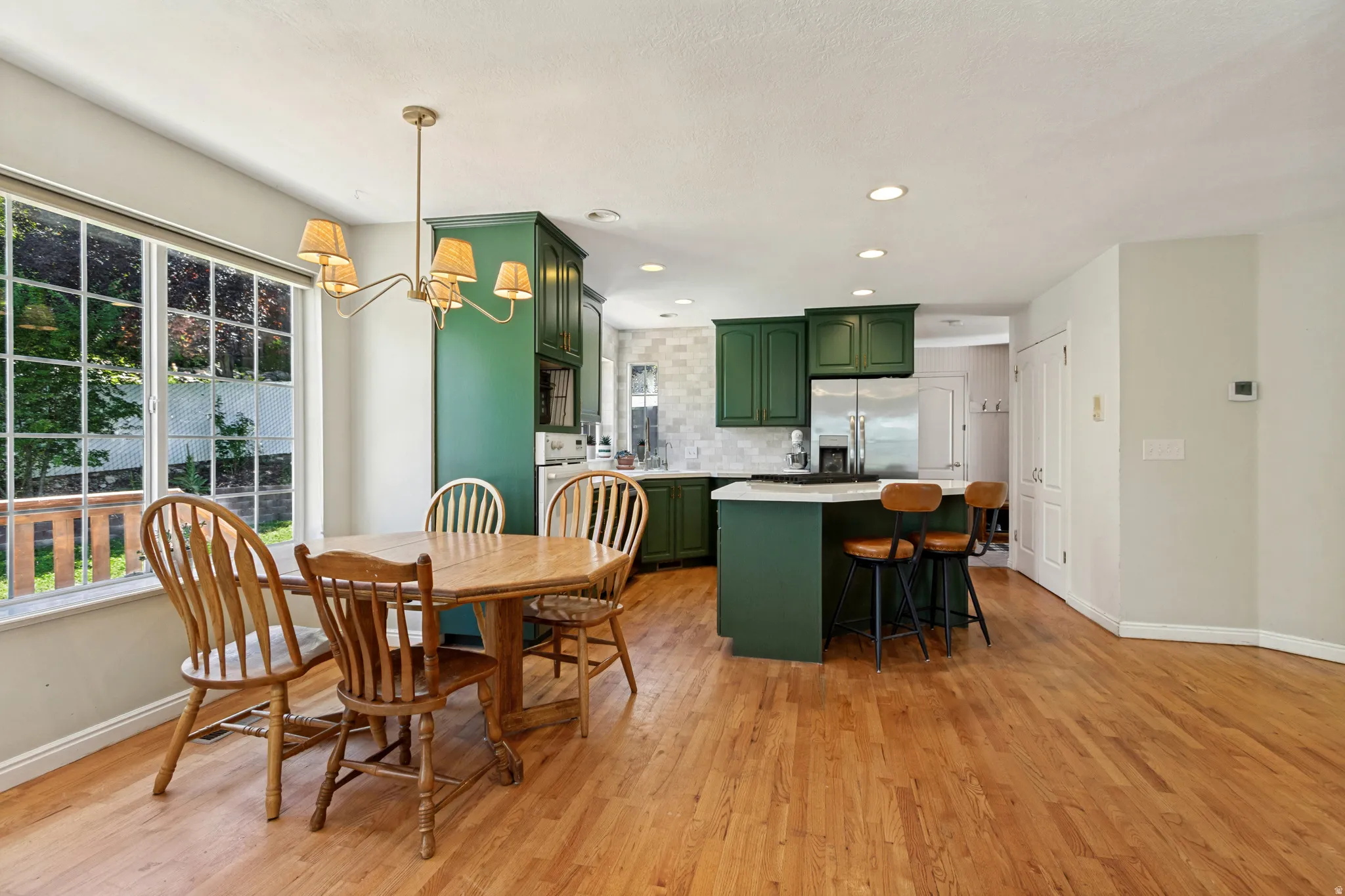 Open-concept kitchen and dining area featuring rich green cabinetry, a central island with counter seating, stainless steel appliances, and wood-finish flooring