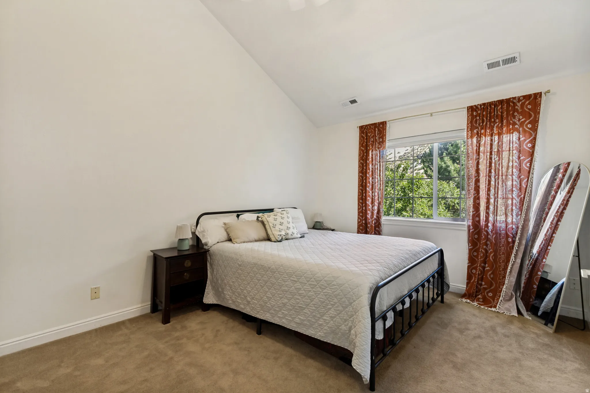 Bedroom featuring vaulted ceilings, a window with exterior tree scenery, beige carpeting, and white baseboards