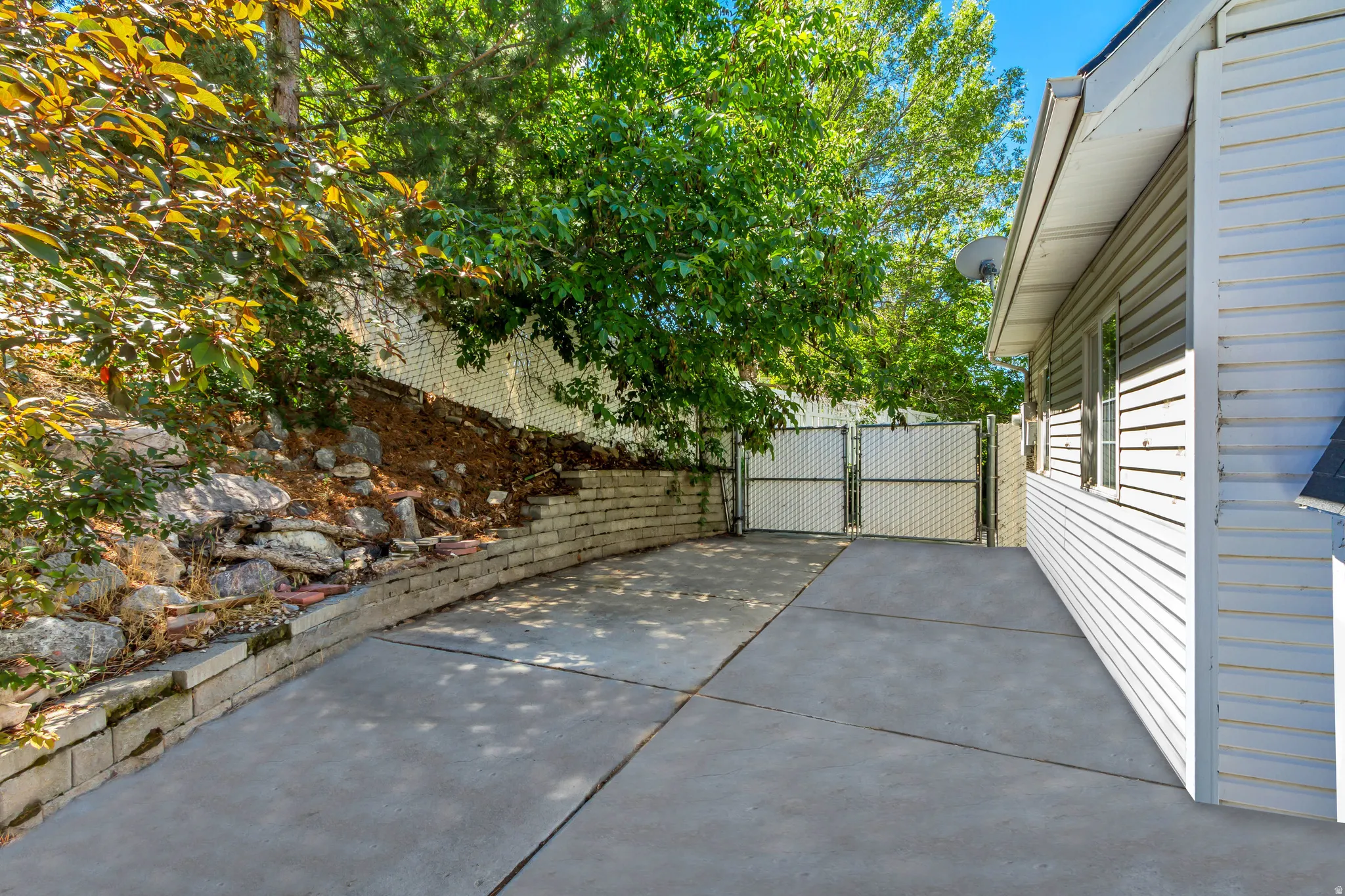 Concrete driveway featuring a metal chain-link gate and a retaining wall