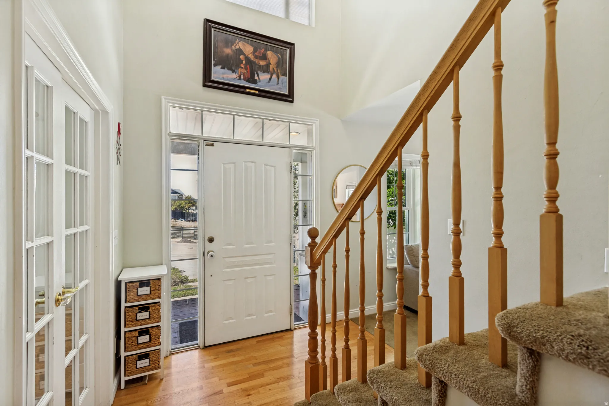 Entryway featuring wood-finish flooring, a white paneled entry door with sidelights and transom window, and a staircase with wood balusters and carpeted treads