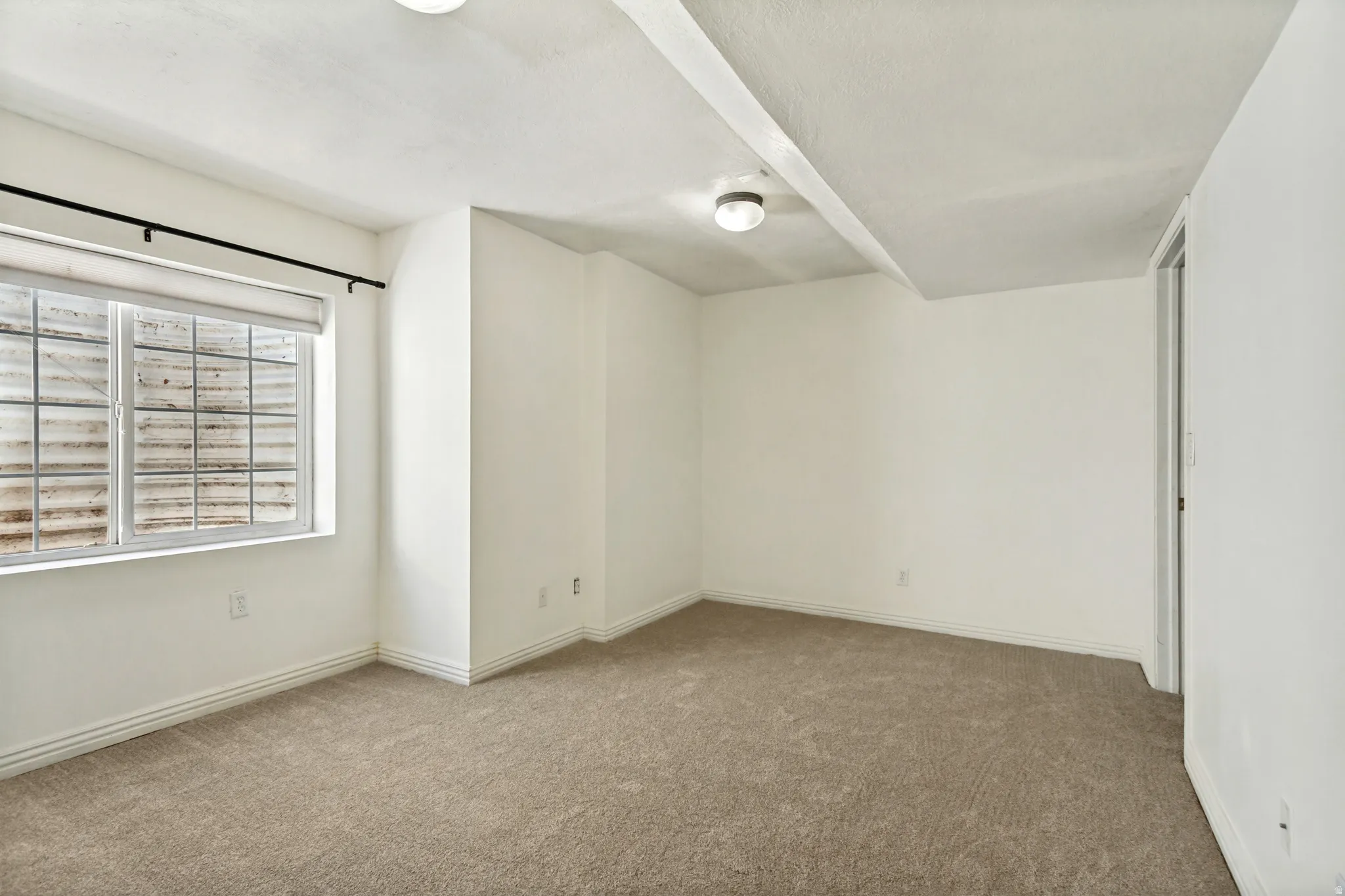 Carpeted room with a double window featuring a window well, overhead lighting, and white baseboards