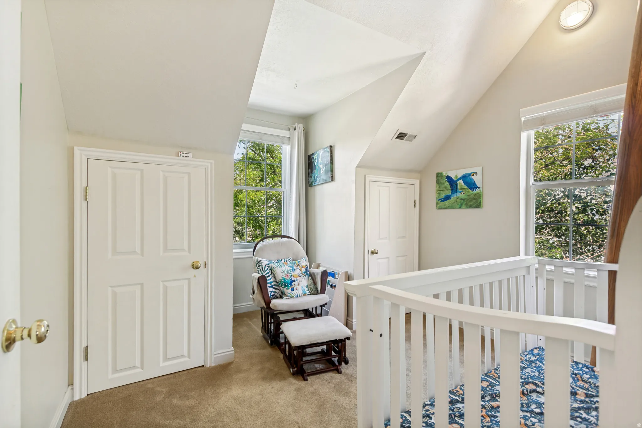 Carpeted room featuring sloped ceilings, two windows with exterior foliage, and two paneled doors with brass hardware