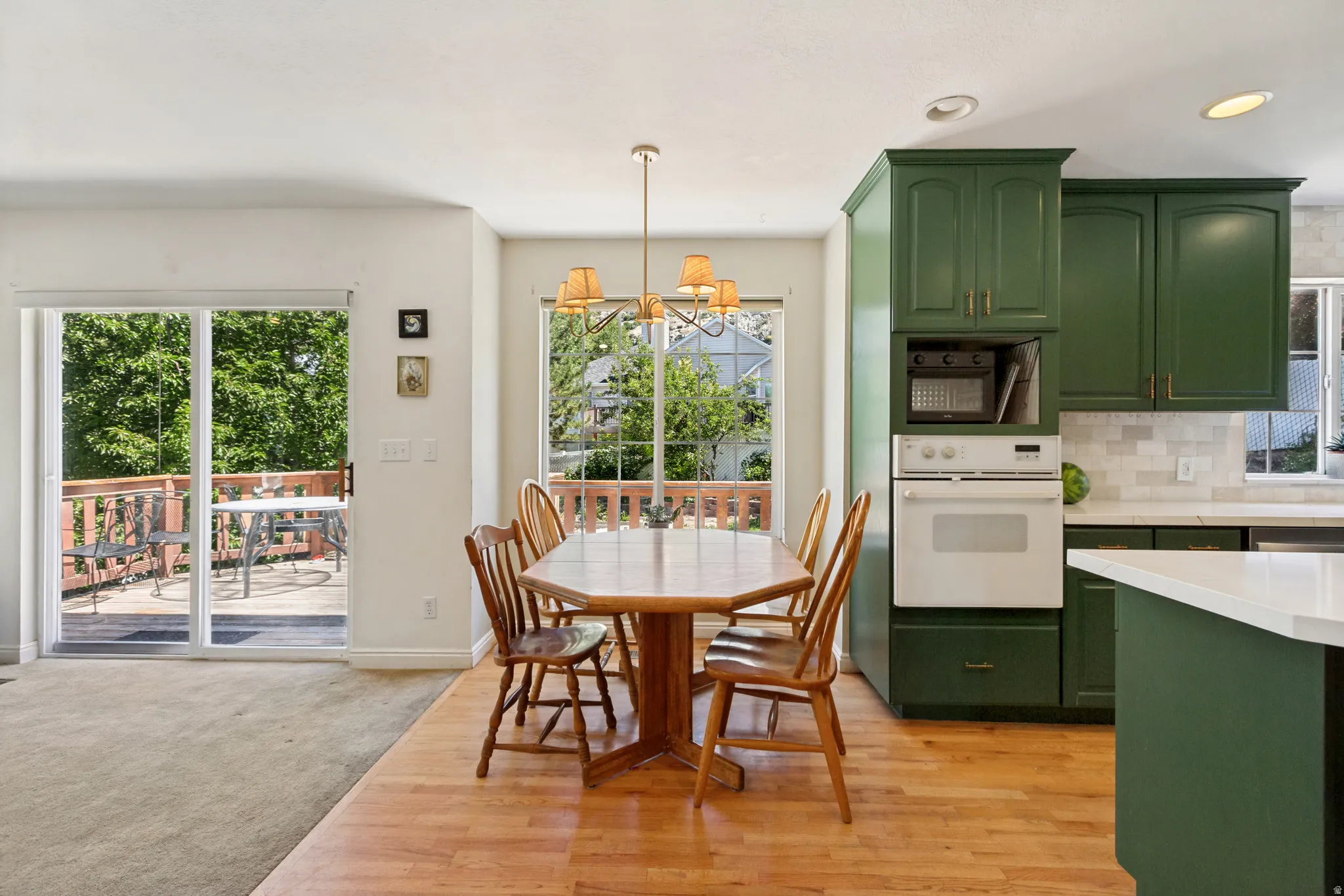 Kitchen and dining area featuring vibrant green cabinetry, white appliances, a built-in oven, and a tile backsplash
