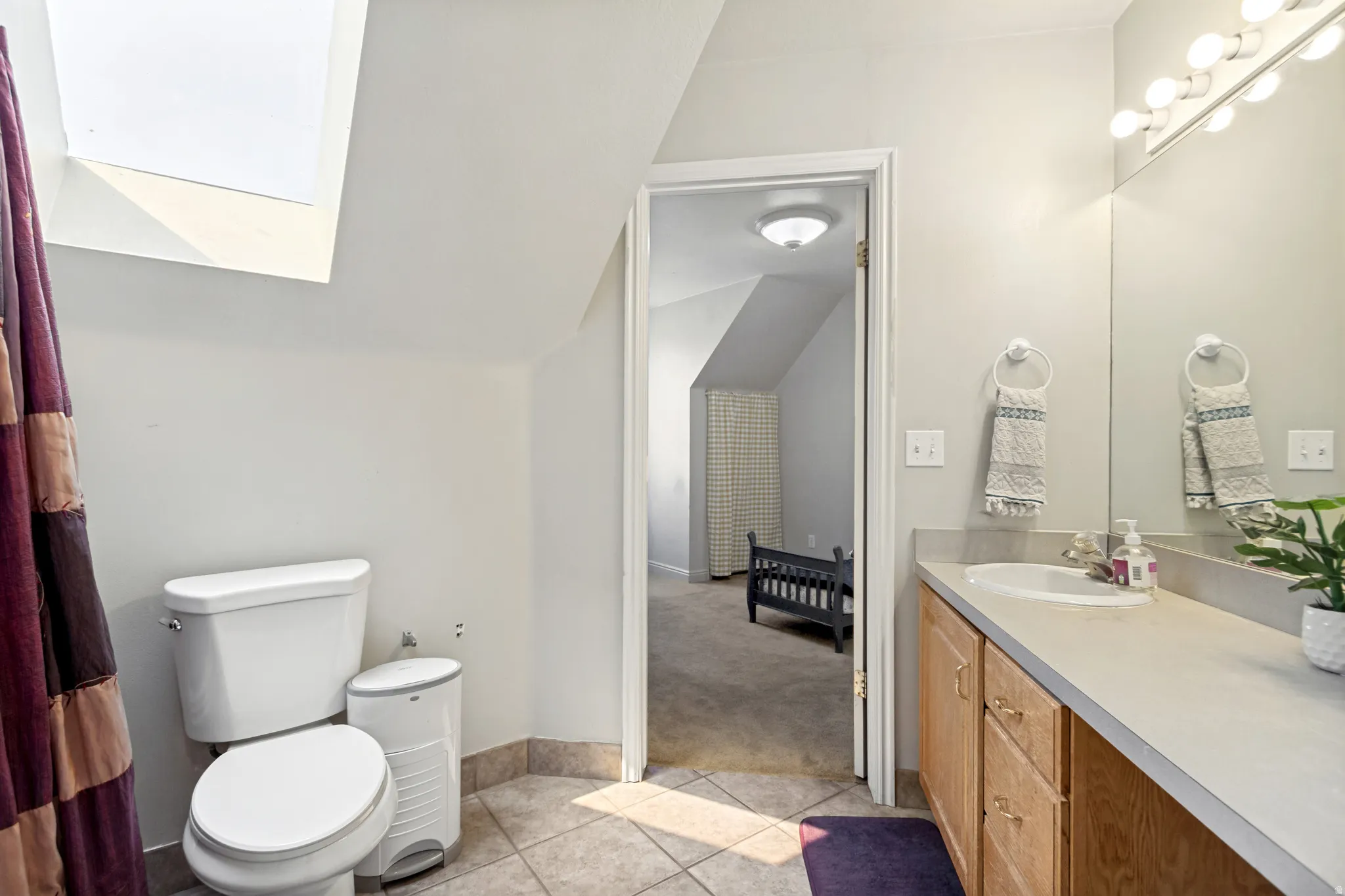Bathroom featuring a skylight, tile flooring, a built-in vanity with wood-finish cabinetry, a single basin sink, and an overhead vanity light fixture