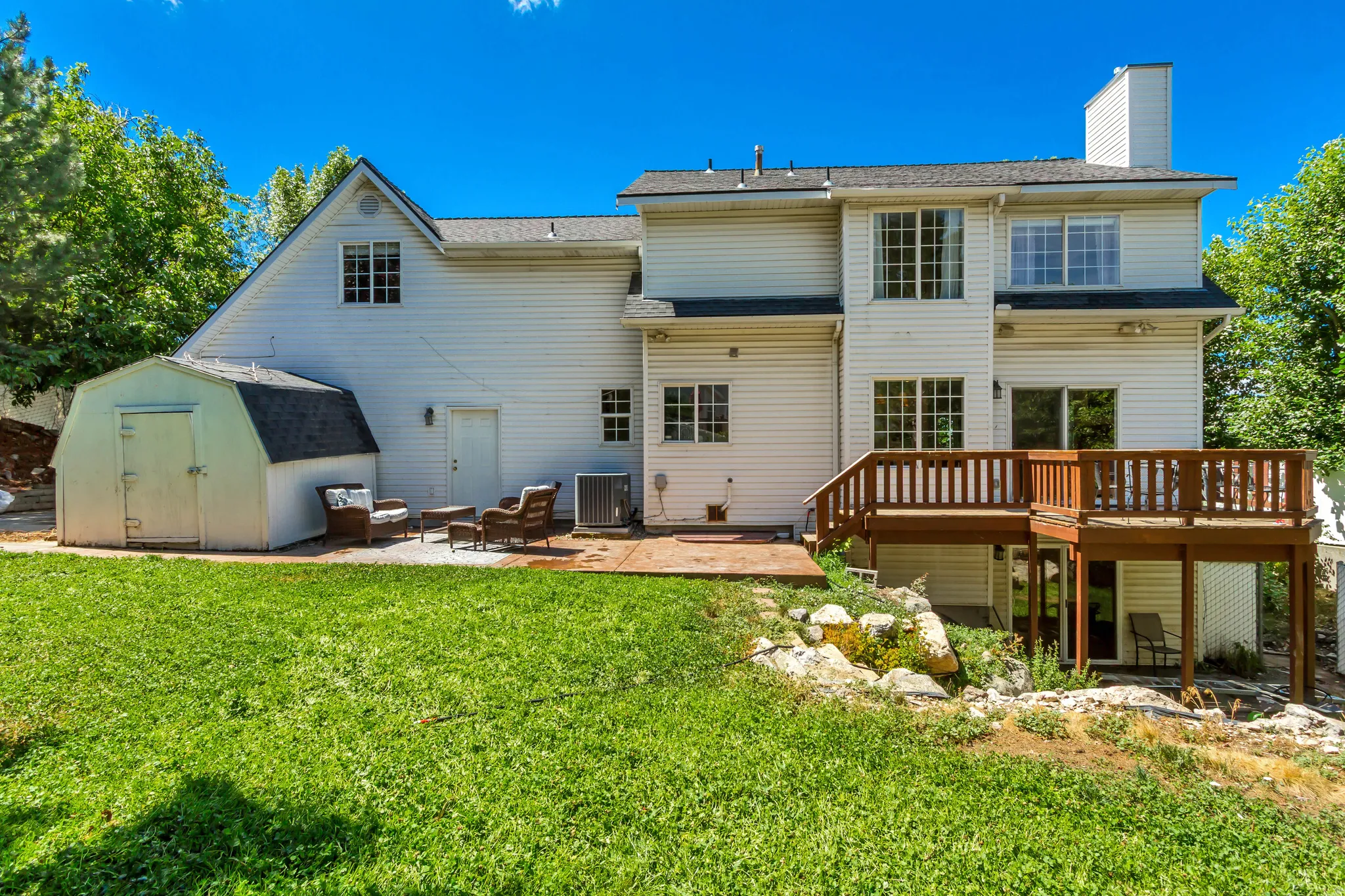 Rear exterior featuring an elevated wood deck, a patio area, a detached storage shed, and a verdant lawn