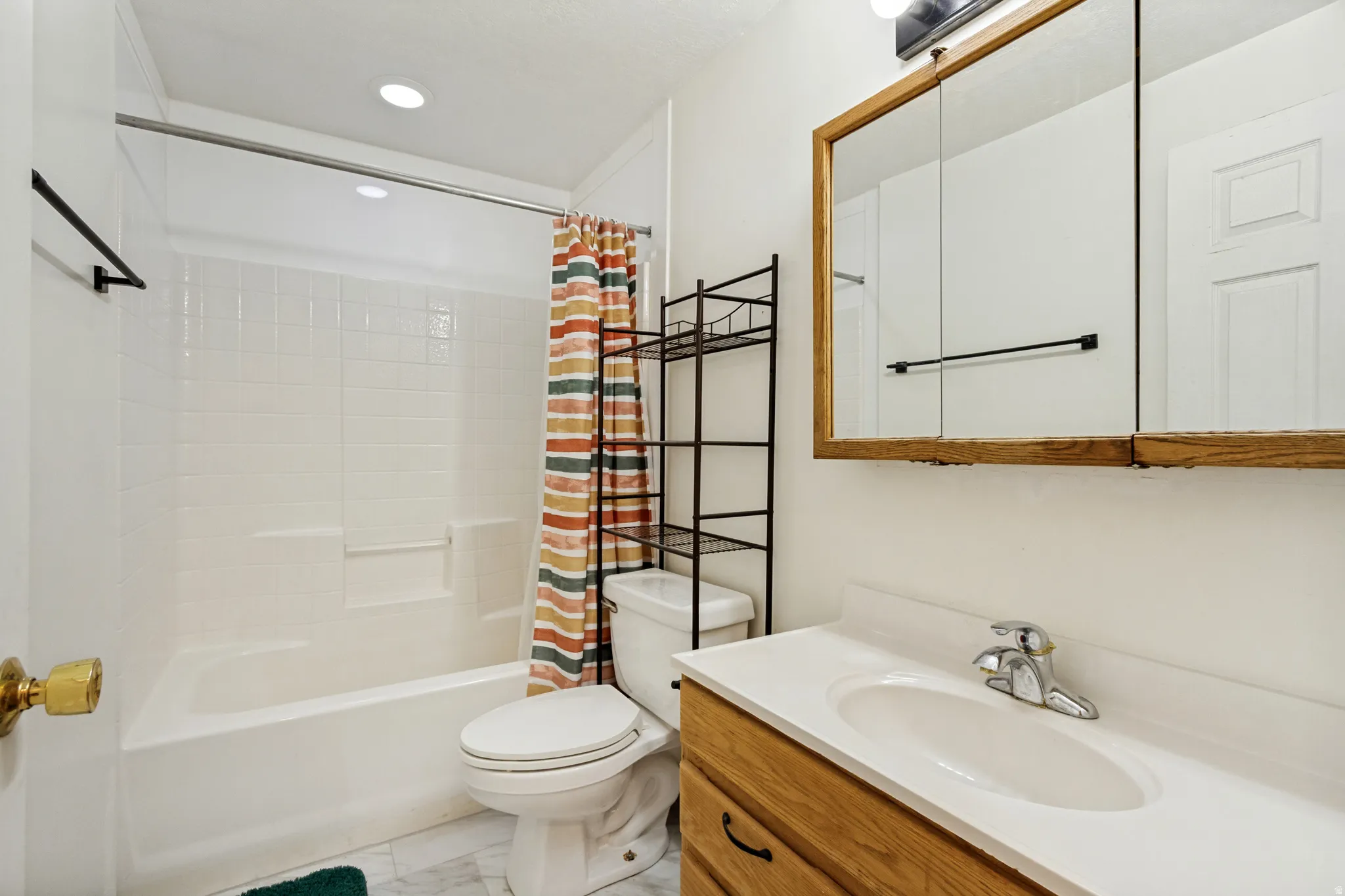 Bathroom featuring a white bathtub and shower surround, a light wood-finish vanity with a white countertop and integrated sink, a matching wood-finish medicine cabinet, and recessed ceiling lighting