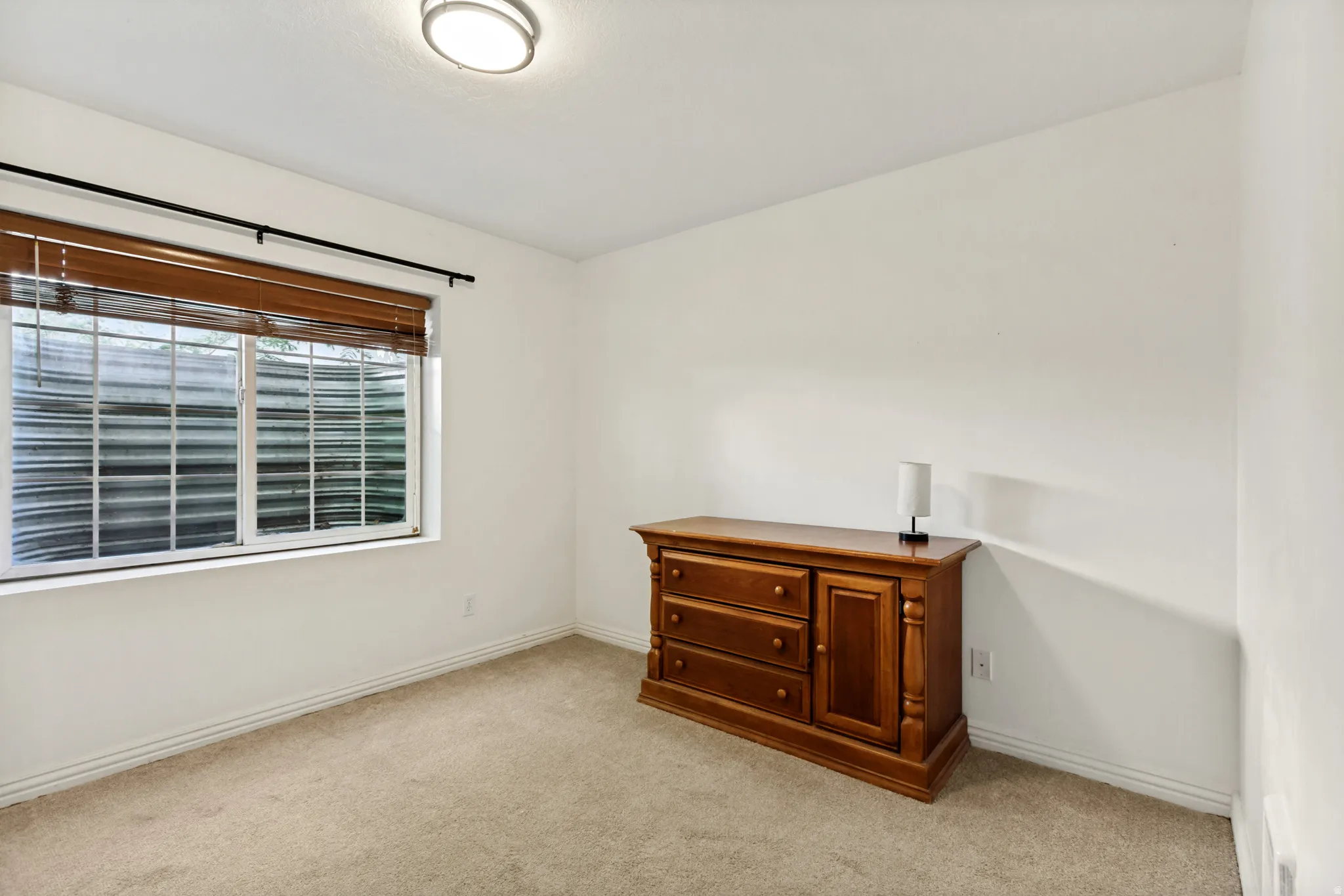 Spacious room featuring neutral carpet flooring, white walls, and a large window with horizontal blinds