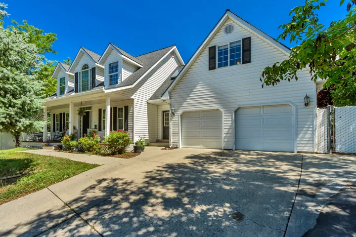 White siding exterior featuring a covered front porch with columns, multiple dormer windows, and a two-car garage