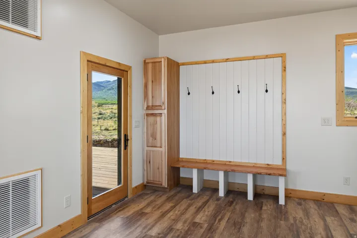 Wood-finish flooring, built-in storage with shaker-style doors, built-in bench with coat hooks, and natural wood trim accents