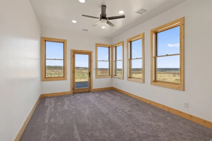 Carpeted room with recessed lighting, ceiling fan, and multiple windows with wood trim