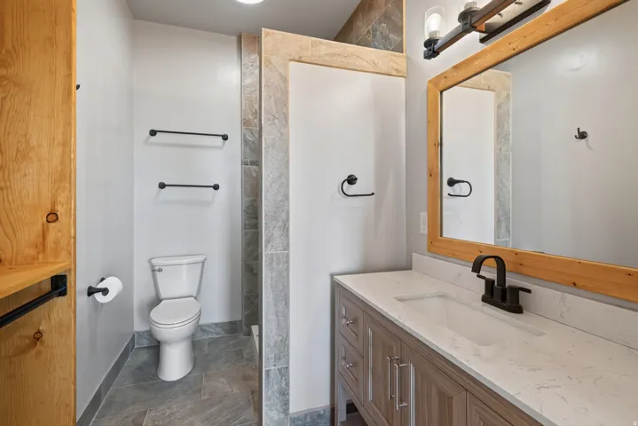 Vanity with a light-toned countertop and an undermount sink, framed mirror with a light wood finish, and dark-toned fixtures