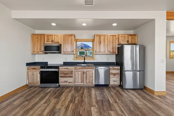 Kitchen featuring wood-finish flooring, recessed lighting, wood cabinetry, dark countertops, and stainless steel appliances