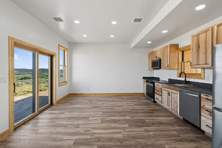 Wood-finish flooring, recessed lighting, and a kitchen featuring wood cabinetry, dark countertops, and stainless steel appliances