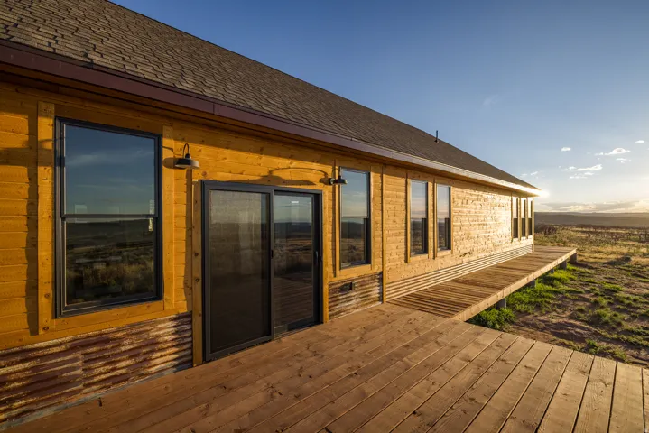 Exterior featuring horizontal wood siding, a wooden deck, multiple windows with dark frames, a sliding glass door, and corrugated metal wainscoting