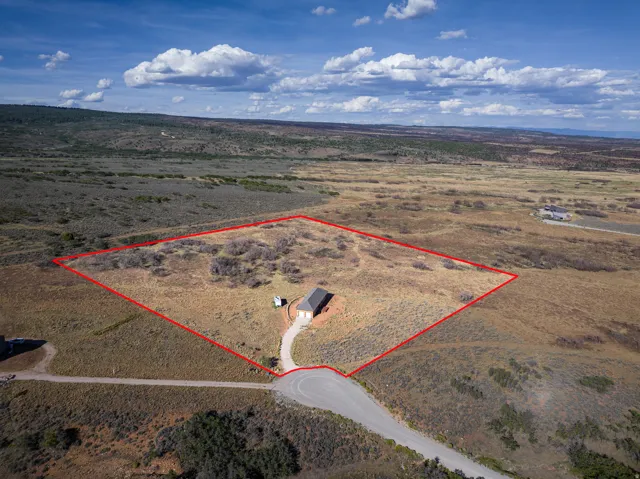 Expansive undeveloped land with a partial paved driveway and a single structure
