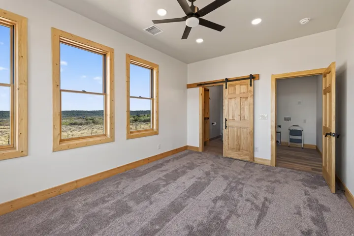 Multiple windows with wood trim, wood-finish flooring, wood barn door, and a ceiling fan with recessed lighting