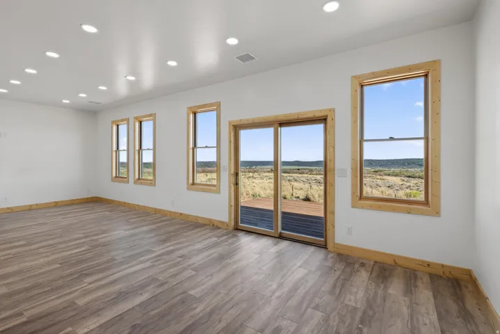 Spacious room featuring recessed lighting, wood-finish flooring, multiple windows with natural wood trim, and a sliding glass door opening to an outdoor deck