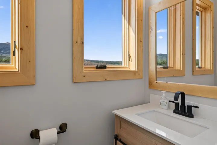 Wood-framed windows, wood-framed mirror, white countertop, integrated sink, and a matte black faucet