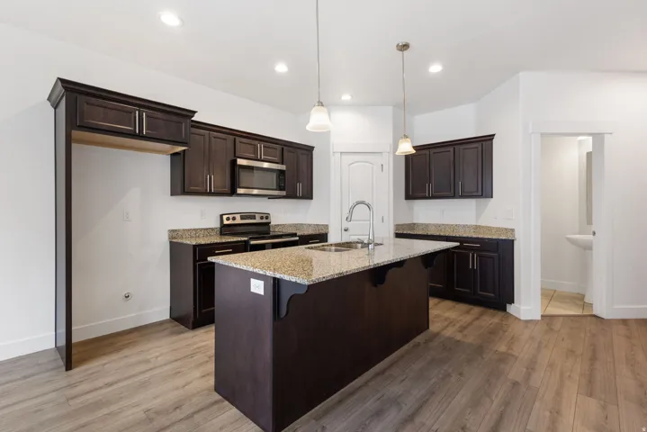 Modern kitchen featuring dark wood cabinetry with brushed nickel hardware, granite countertops, and wood-finish flooring