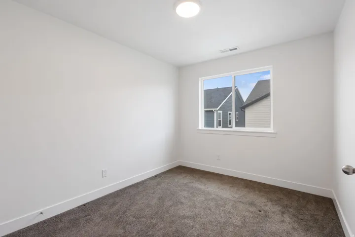 Carpeted room featuring a white ceiling and walls, a centered window with white trim, and a flush-mount ceiling light fixture
