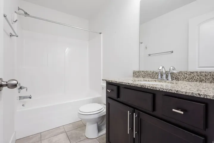 Bathroom featuring a dark wood-finish vanity with a light-colored speckled countertop, a large wall-mounted mirror, a white toilet, and a white tub/shower combination