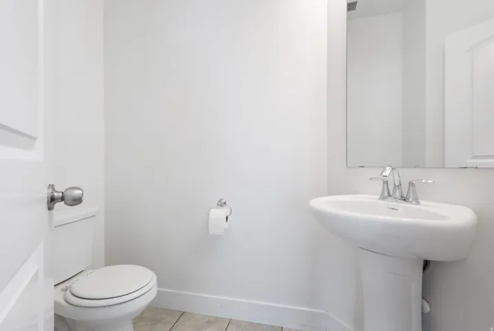 Bright powder room featuring a pedestal sink with chrome faucet, a rectangular wall-mounted mirror, and neutral wall paint