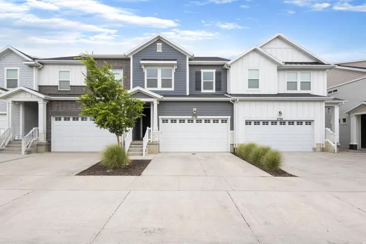 Modern townhome exterior featuring a two-car garage, gray horizontal siding, white trim, and a covered entry