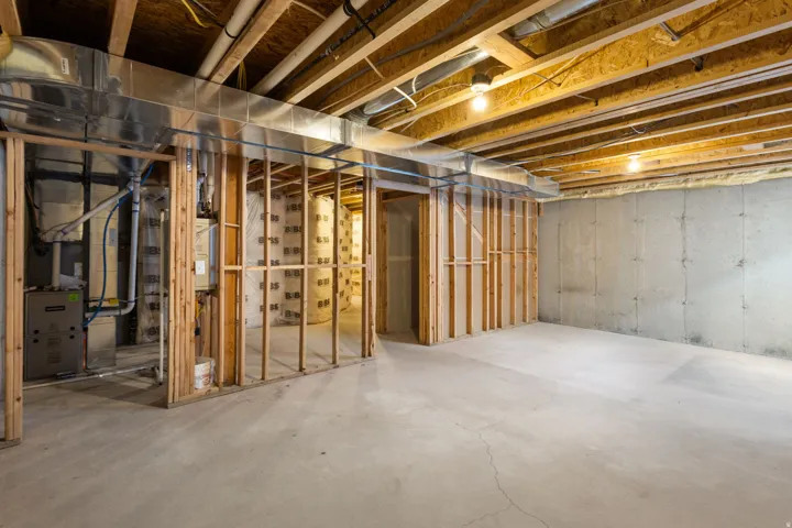 Unfinished basement featuring concrete flooring, exposed wood ceiling joists, and framed partition walls