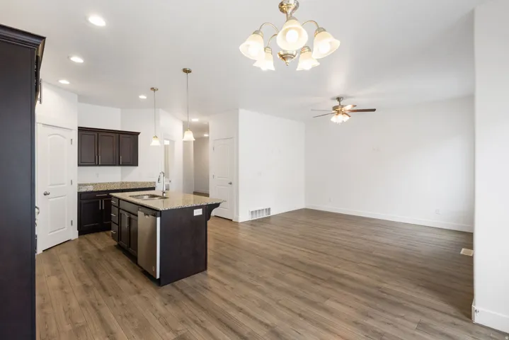 Open-concept living space featuring wood-finish flooring, a kitchen island with integrated sink, stainless steel dishwasher, and recessed lighting