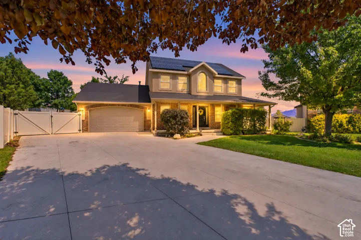 Two-story residence featuring brick and siding exterior, expansive concrete driveway, attached garage, integrated solar panels, and arched window detailing