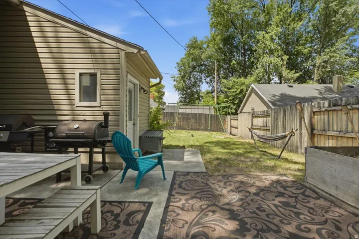 Expansive backyard featuring a concrete patio, mature trees, a wooden privacy fence, and a storage shed