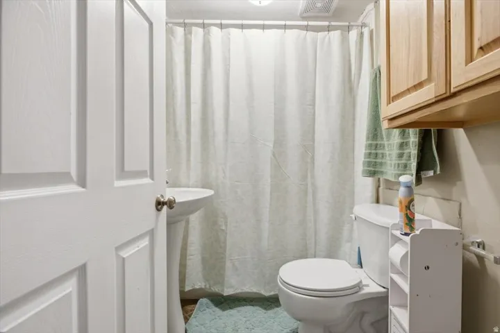 Pedestal sink with white basin, white toilet, and natural wood cabinetry