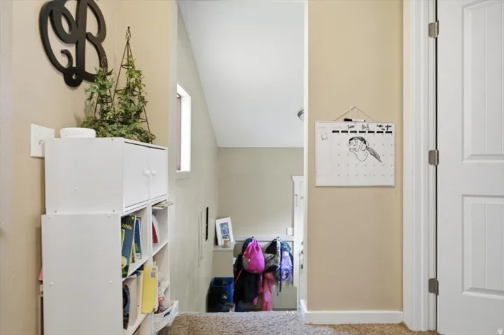 Hallway with a neutral wall color, white trim, and textured carpet flooring