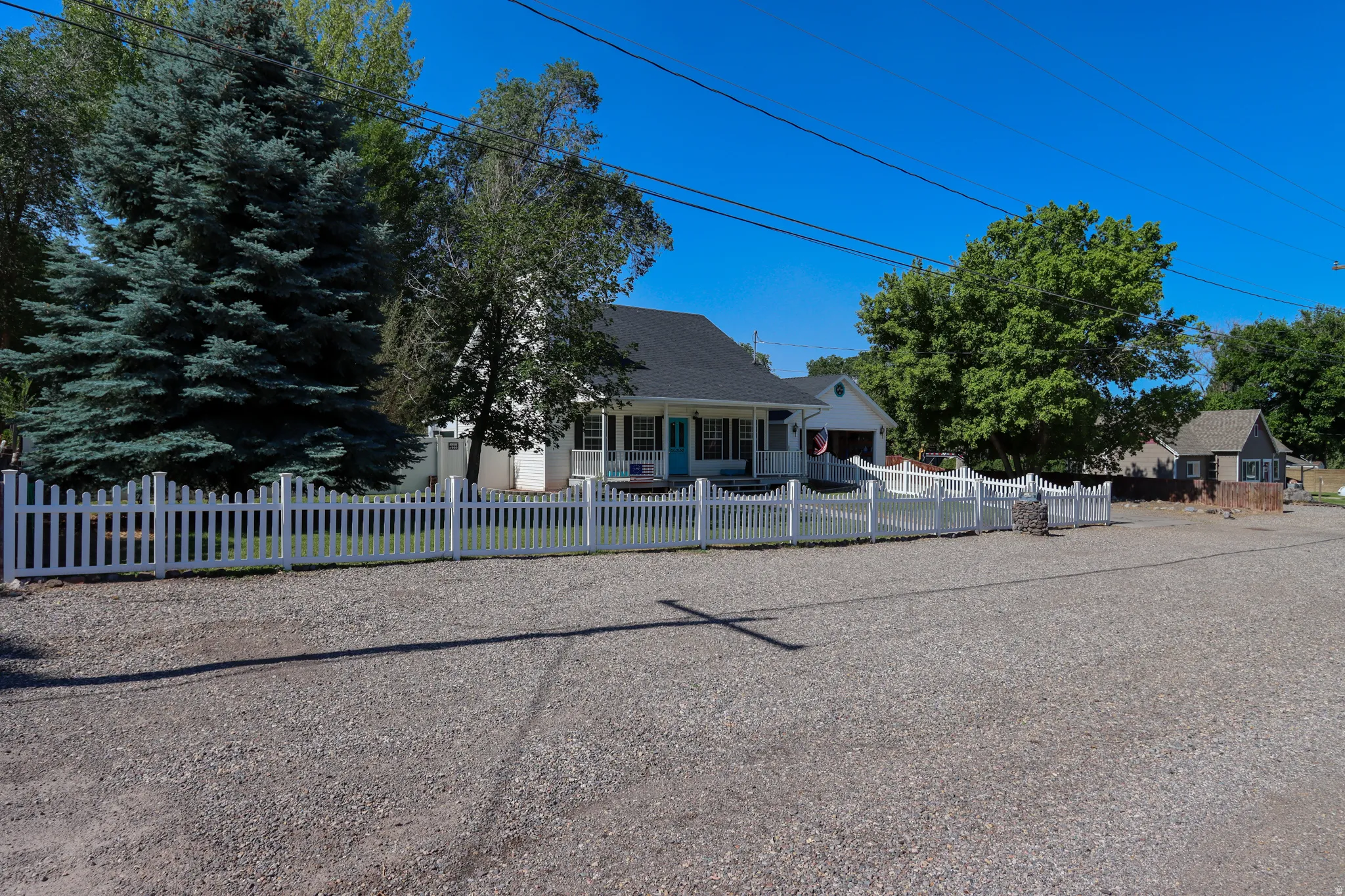 White picket fence enclosing a landscaped front yard with a mature evergreen tree