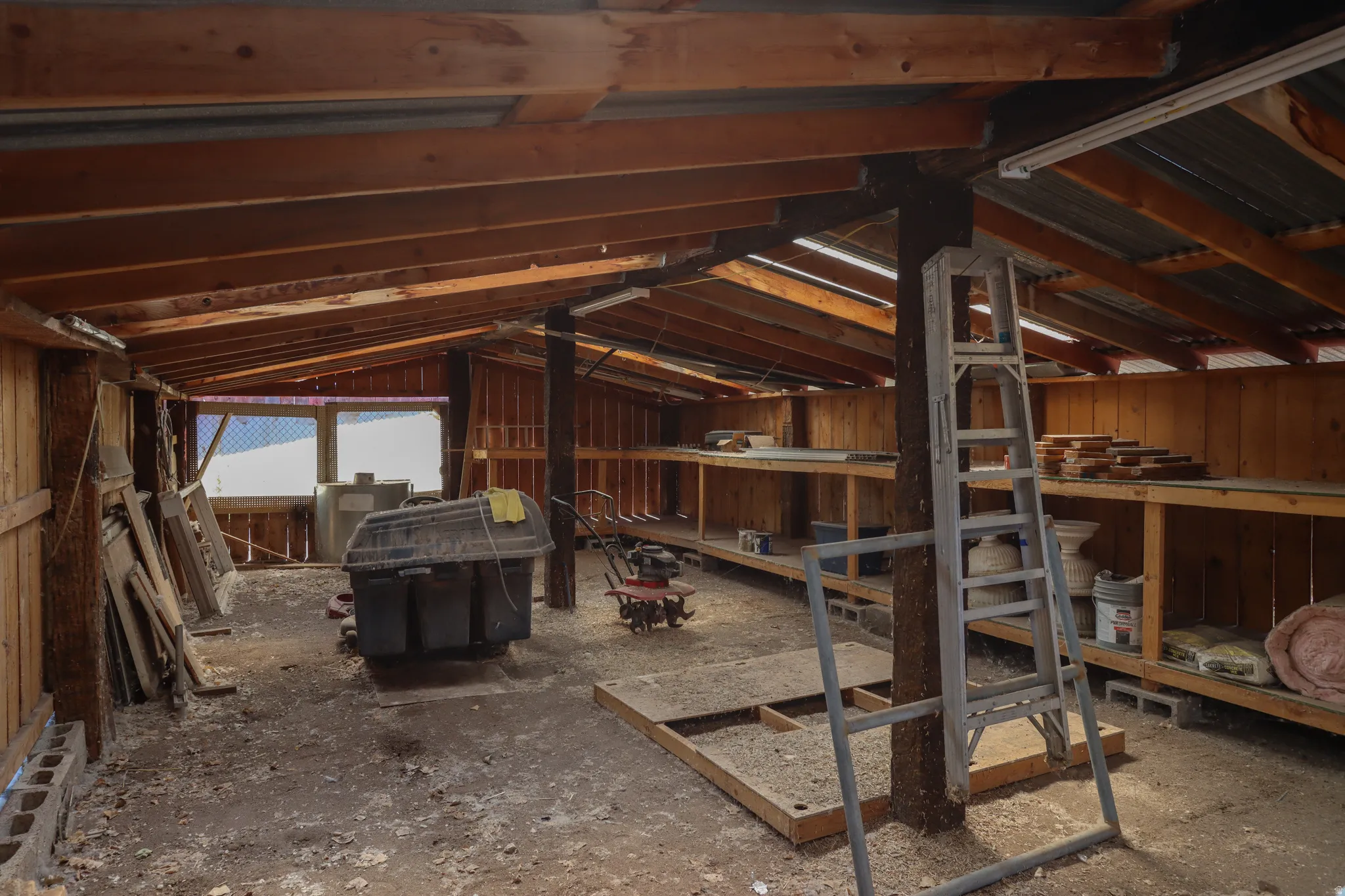 Spacious utility structure featuring exposed wood beams, a corrugated metal roof, built-in shelving, and multiple windows providing natural light