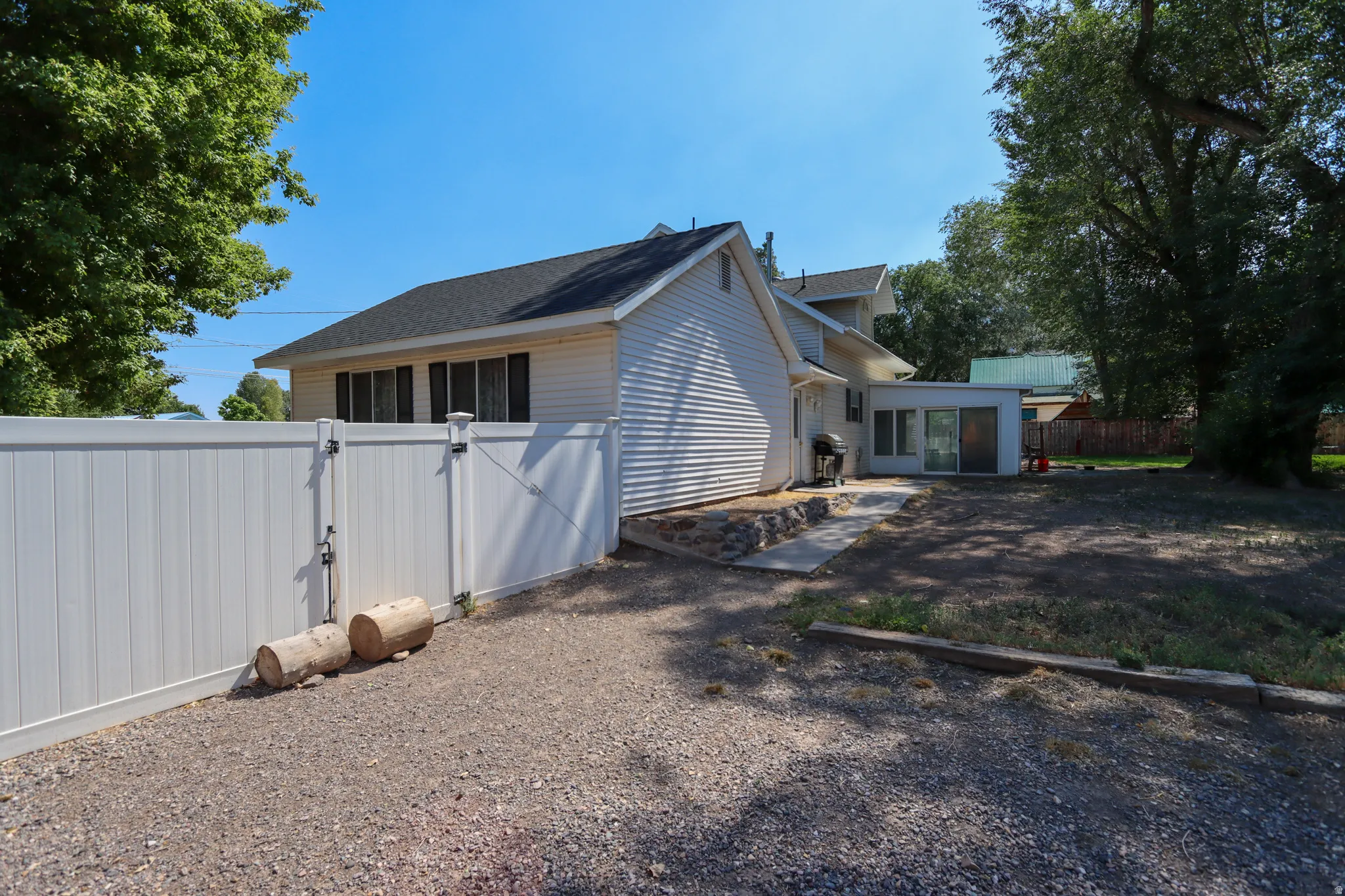 White vinyl privacy fence enclosing a gravel parking area and a partially cleared yard