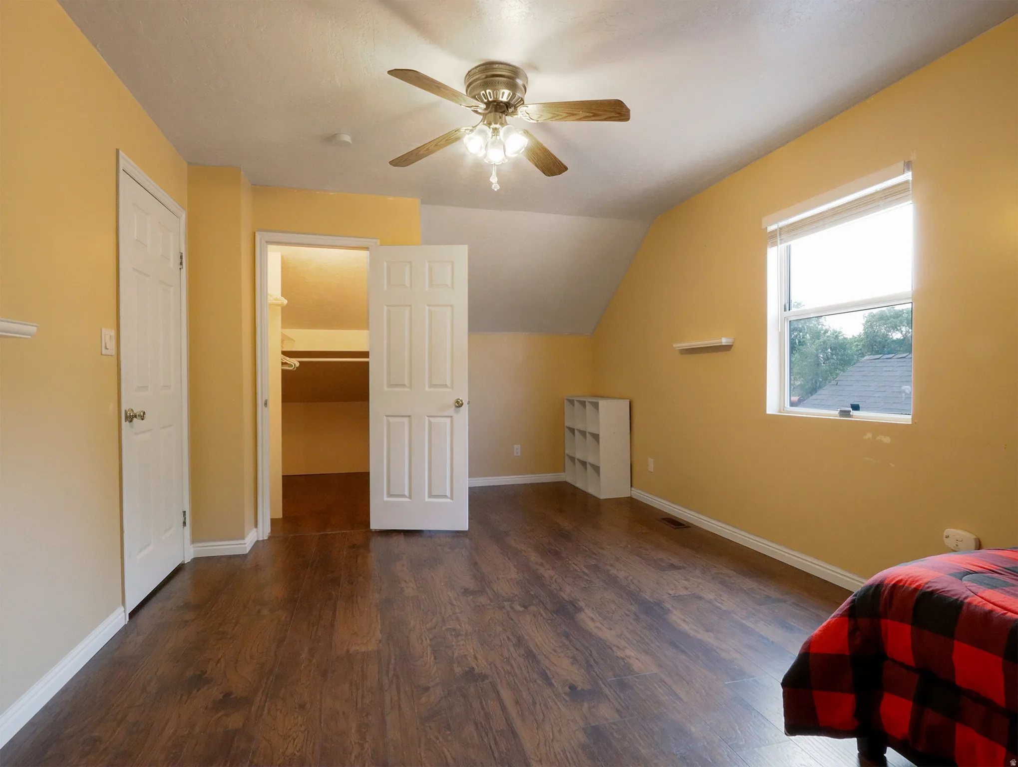 Spacious room featuring wood-finish flooring, a ceiling fan with integrated lighting, and a window with blinds