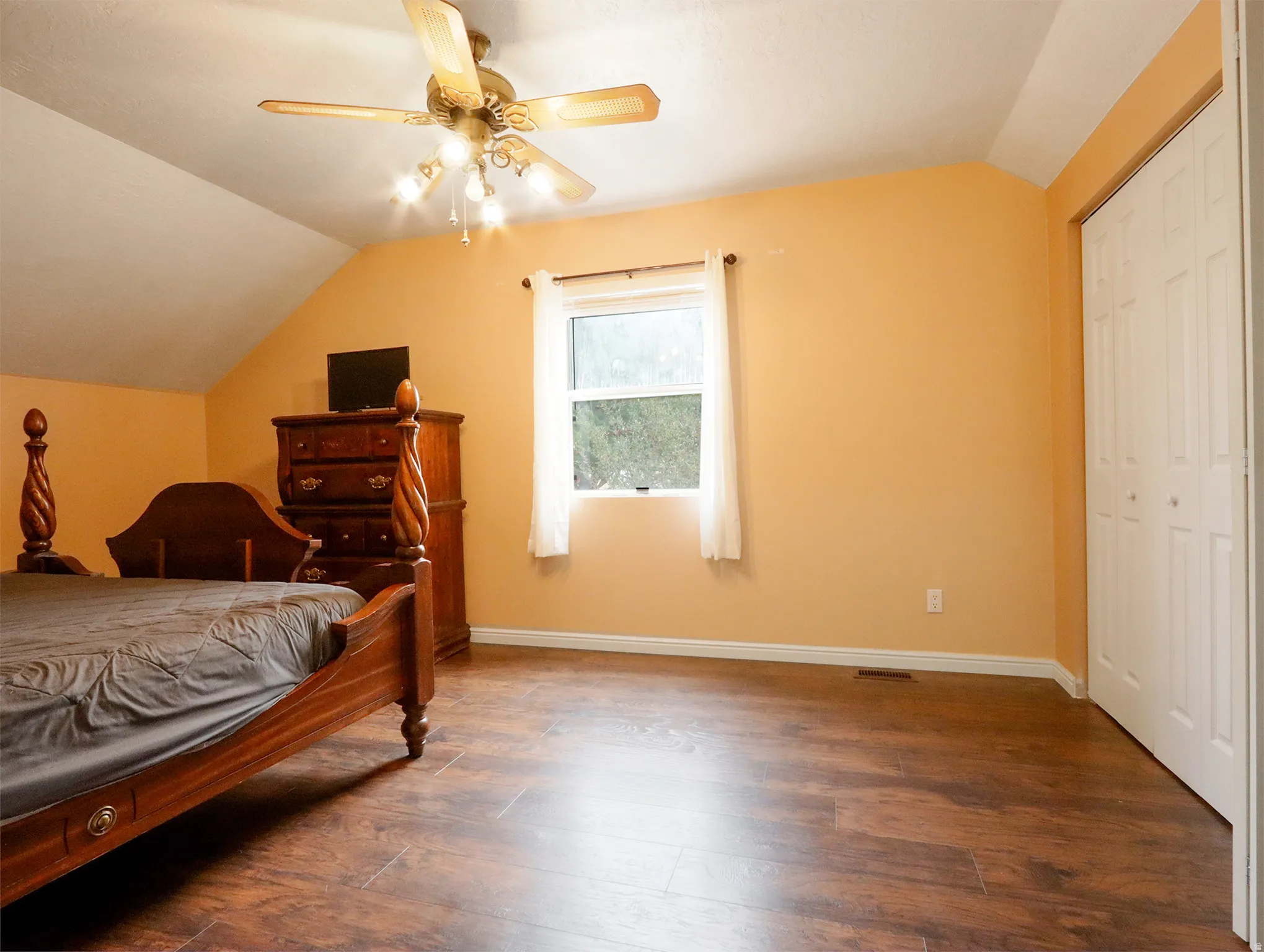 Room featuring wood-finish flooring, a ceiling fan with integrated lighting, and a window with white curtains