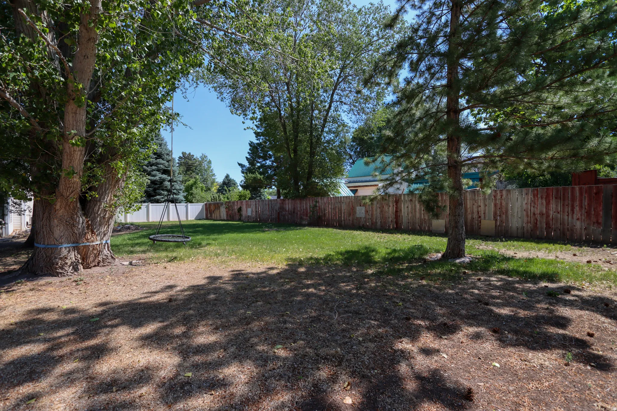 Expansive backyard featuring a manicured lawn, mature trees, and a surrounding privacy fence